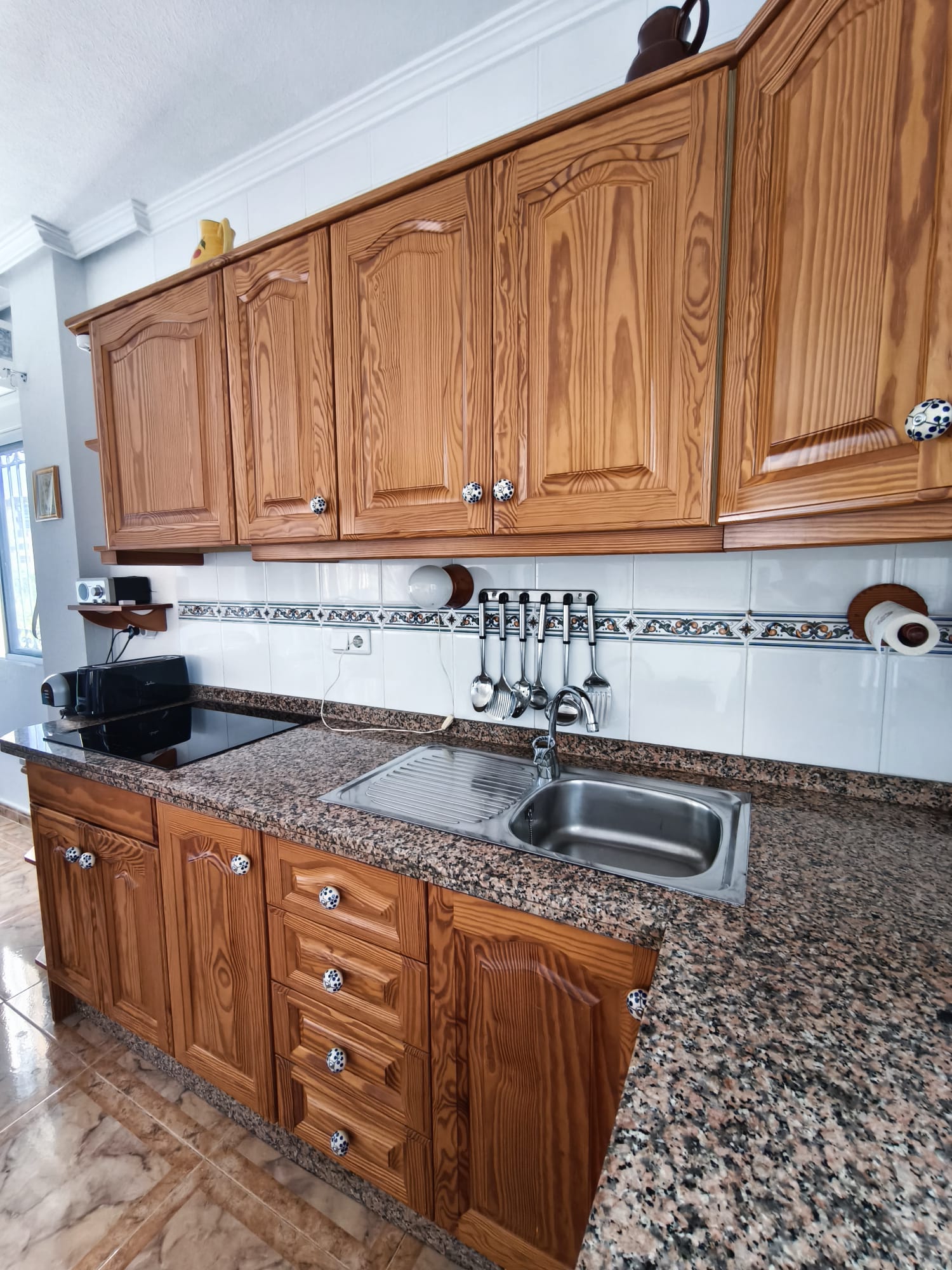 Full kitchen view with pine cabinets, granite countertop, sink, coffee machine, and utensils