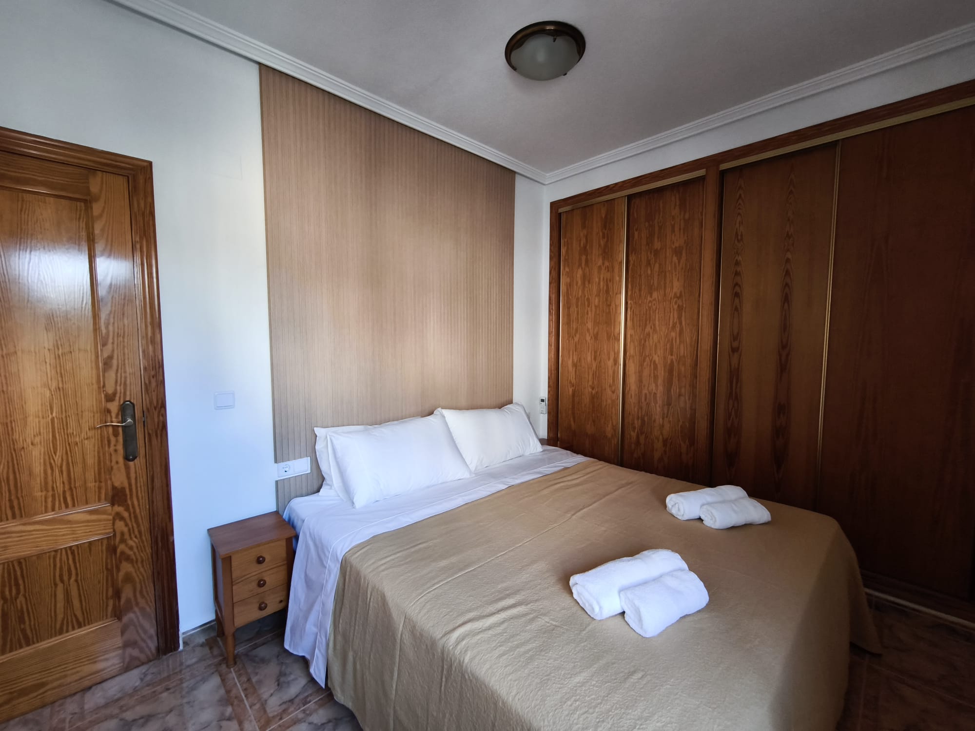 Double bedroom with large wooden wardrobe, headboard, and fresh towels