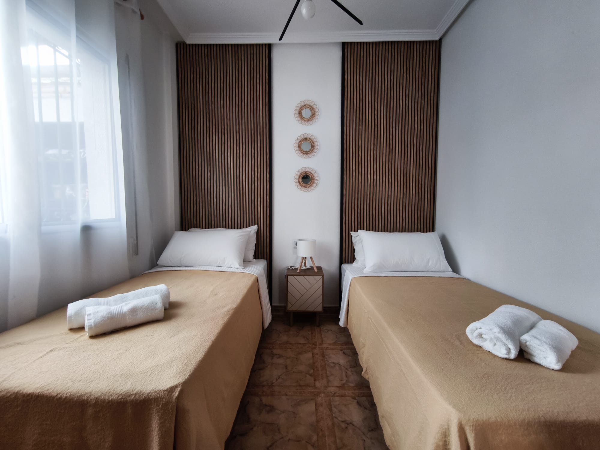 Twin bedroom with modern wood slat panels, decorative mirrors, and fresh towels