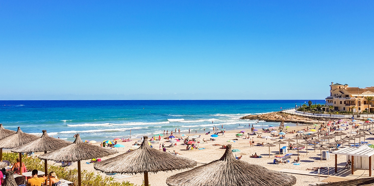 La Zenia Beach with crystal-clear Mediterranean waters, golden sand, and thatched parasols