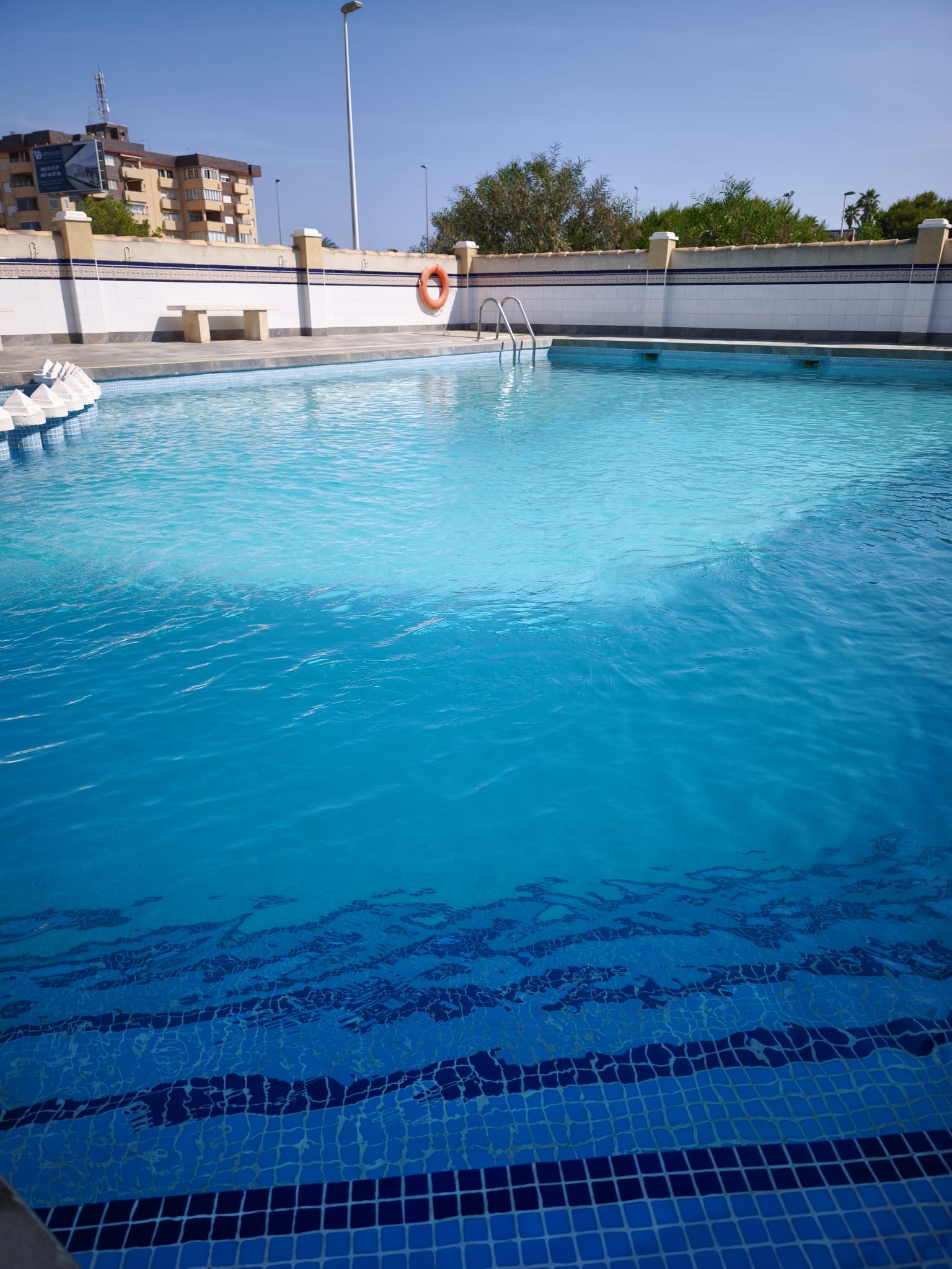 Crystal-clear community swimming pool with ladder, life ring, and tiled surround