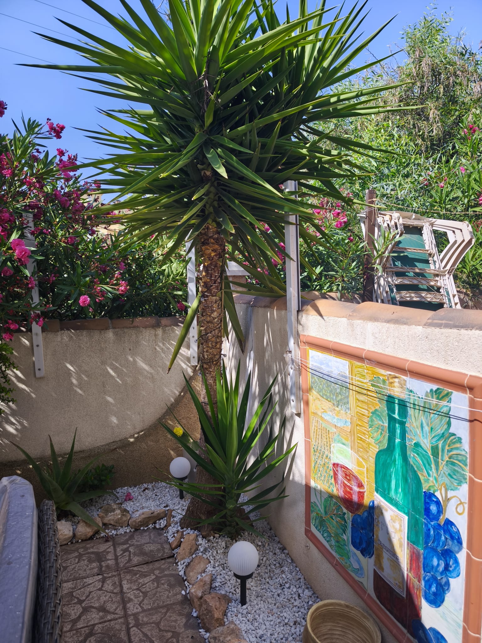 Garden corner with yucca palm, colorful decorative tile mural, flowering oleander, and garden lights