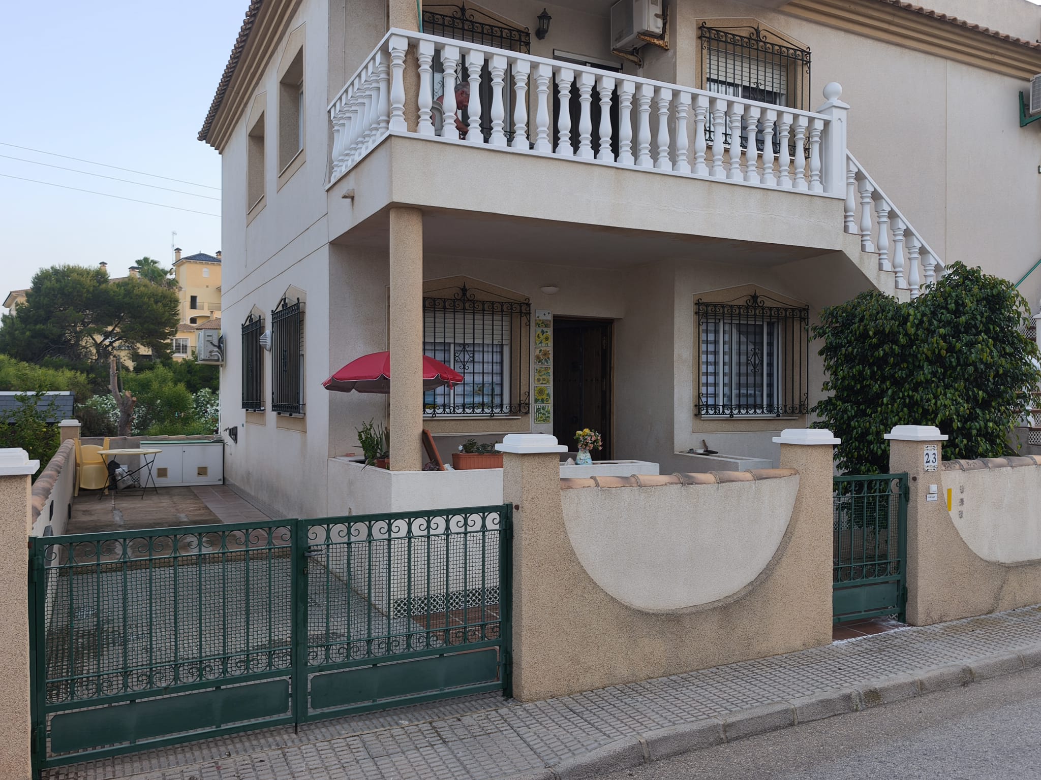 Building exterior from street with green gates, covered porch, wrought-iron grilles, and upper balcony with white balustrade