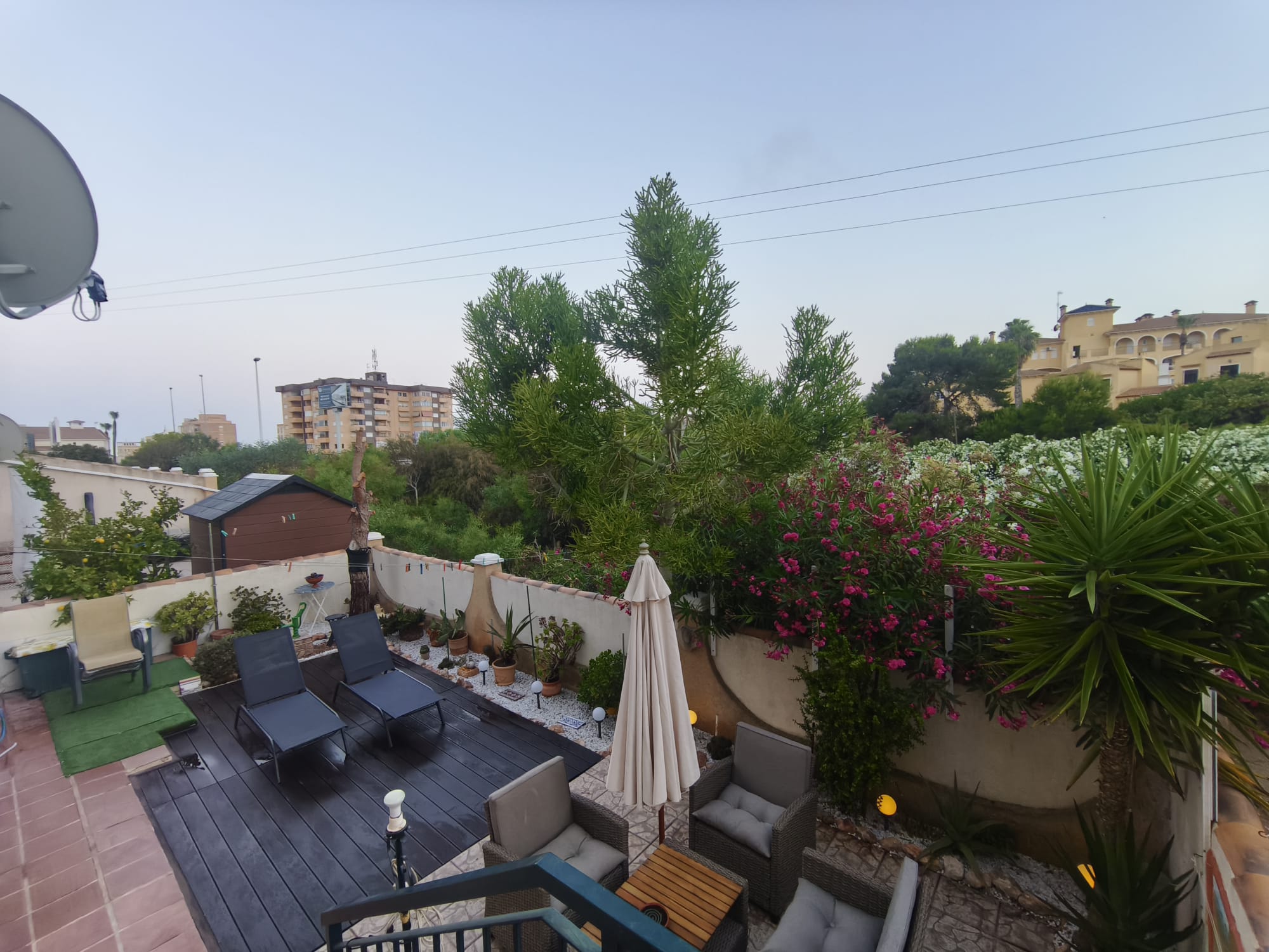 Terrace from above with sun loungers on composite decking, rattan seating area, flowering oleander, and neighborhood views